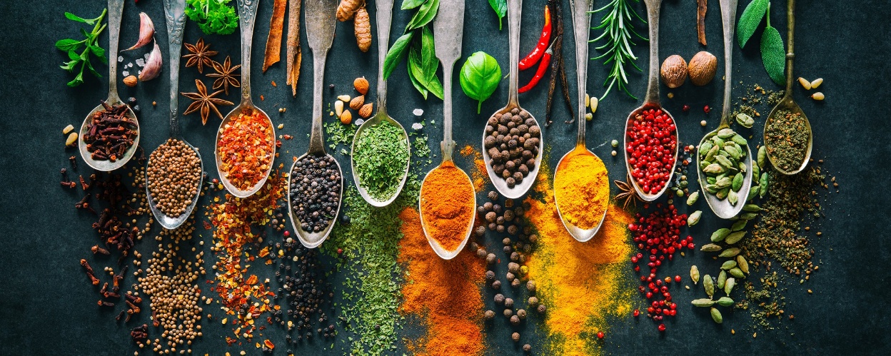 Viele Löffel mit bunten Gewürzen nebeneinander auf einer Schieferplatte dargestellt