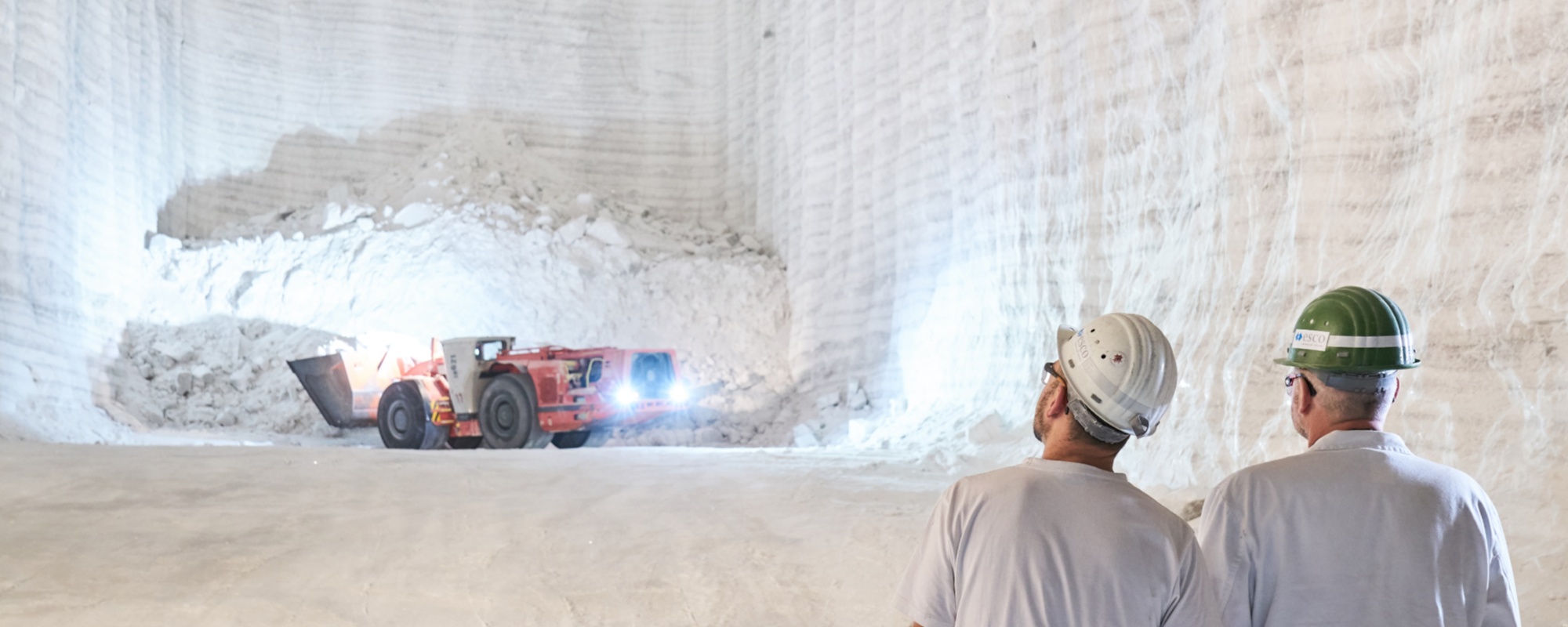 Untertagewelt, roter Radlader mit Schaufel, zwei Mitarbeiter in Schutzkleidung